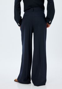 Pantalones de pierna ancha azul marino con sutiles rayas verticales, que cuentan con una cinturilla ajustada y dos bolsillos traseros, fabricados en una tela suave.