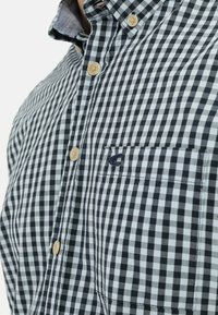 Camicia a quadretti bianco e nero con colletto button-down, con bottoni beige e taschino sul petto con dettagli ricamati.