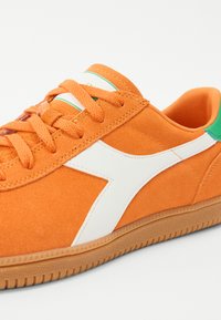 Oranje suede sneaker met witte accenten en een groene hiel, voorzien van platte veters, een textuur rubberen zool en een gladde binnenvoering.