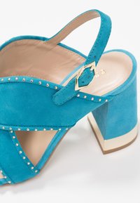 Aqua suede korkokengät, joissa on ristiin menevät hihnat, koristeelliset hopeasuikaleet ja neliömäinen kultasävyinen korko.
