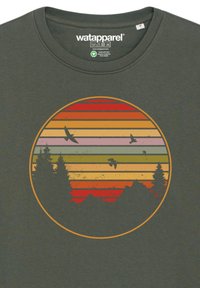 Donkergroene T-shirt met een cirkelvormige grafiek met horizontale strepen in rood, oranje, roze, groen en geel, die bomen en vliegende vogels afgebeeld.