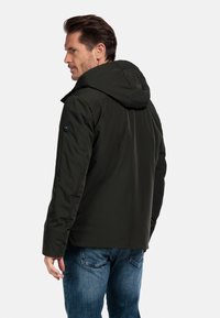 Donkergroene waterdichte jas met capuchon, met een zachte textuur en een zwart logo-embleem op de linkermouw. Casual ontwerp, met ritsluiting.