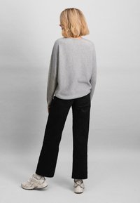 Maglione grigio a maniche lunghe, vestibilità comoda; abbinato a pantaloni neri a gamba dritta e sneakers chiare. Design minimalista, colori neutri.