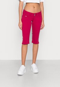 Pantalones capri fucsias de algodón con dos bolsillos delanteros, cierre de dos botones y un corte ajustado, combinados con zapatillas de plataforma blancas.