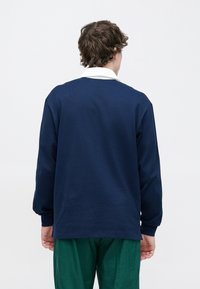 Tengerészkék hosszú ujjú pulóver fehér gallérral, texturált anyagból. Laza szabású, az alsó szegély a derék alatt ér véget.