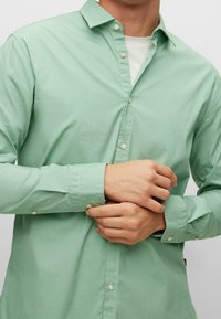 Camicia verde chiaro con maniche lunghe e bottoni a perla. Presenta un colletto a punta e un tessuto leggero e liscio.