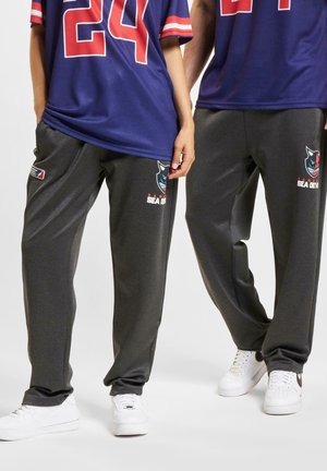 Grå sweatpants med sidelommer, prydet med et logo design og teksten "HANAU SEA DEVILS," kombineret med hvide sneakers.