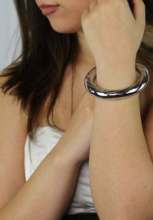 Bracciale in metallo argentato con una superficie liscia e brillante. Forma circolare con un design senza cuciture, indossato sul polso di una persona.