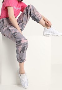 Rosa kamouflage cargobyxor med elastiska manschetter, tillsammans med vita sneakers. Toppen är en figurnära rosa T-shirt med grafiskt tryck.