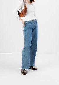 Biała bluzka z długim rękawem z guzikami henley, jasnoniebieskie szerokie dżinsy, brązowa skórzana torebka; czarne i brązowe baleriny w wzory.