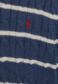 Pull en maille bleue avec des rayures blanches et un petit logo rouge brodé. Présente un tissu texturé et un design épais.