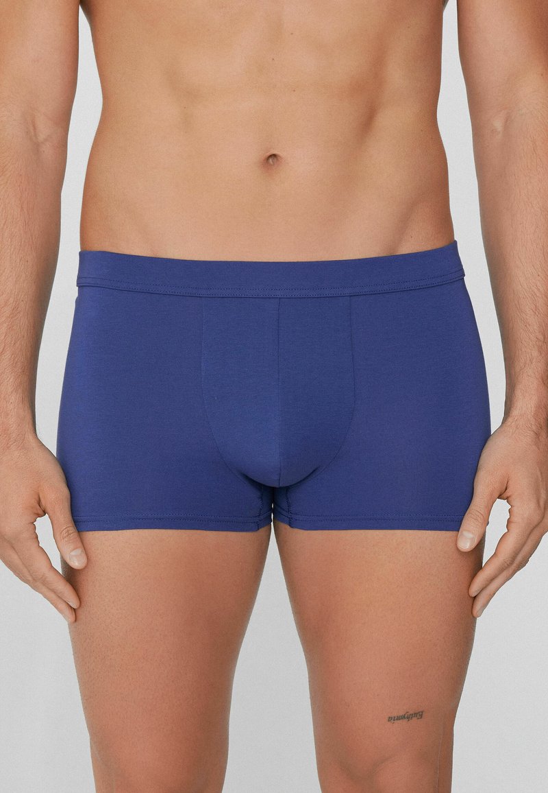 Modré boxerky vyrobené z měkké tkaniny s hladkým povrchem. Mají přiléhavý střih a široký elastický pas. Žádné viditelné vzory ani akcenty.