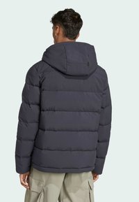 Puff jakna tamnoplave boje s kapuljačom i vodoravnim prošivenim uzorkom. Mekani tekstura s nevidljivim šavovima i minimalnim detaljima hardvera.