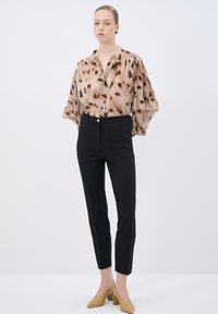 Animal-print blouse with ruffled sleeves, button front; black tailored pants; beige high-heel shoes; neutral background.