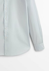 Camicia a maniche lunghe azzurro chiaro realizzata in tessuto morbido, con chiusura a bottoni sul davanti e orlo arrotondato. I polsini sono abbottonati ai polsi.