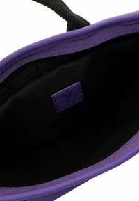 Violet rankinė su tekstūruotu išoriniu paviršiumi, juodu vidiniu pamušalu ir maža, prekiniu odiniu žymeniu. Lygūs kraštai ir tvirti rankenų.