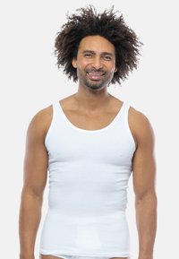 Top in cotone bianco con texture a coste, caratterizzato da spalline larghe e un design aderente, indossato da una persona con capelli ricci.