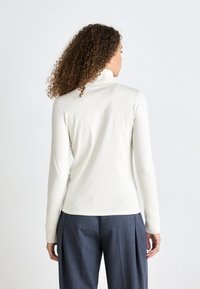 Cremfarbener Rollkragenpullover mit langen Ärmeln und gerippten Bündchen, kombiniert mit dunkelblauen, weit geschnittenen Hosen. Glatte Textur, enganliegendes Design.