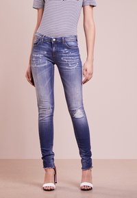 Verblasste blaue Skinny-Jeans aus Baumwollmischung, mit abgetragenen Akzenten und fransigen Säumen, kombiniert mit einem gestreiften Oberteil und offenen Schuhen.