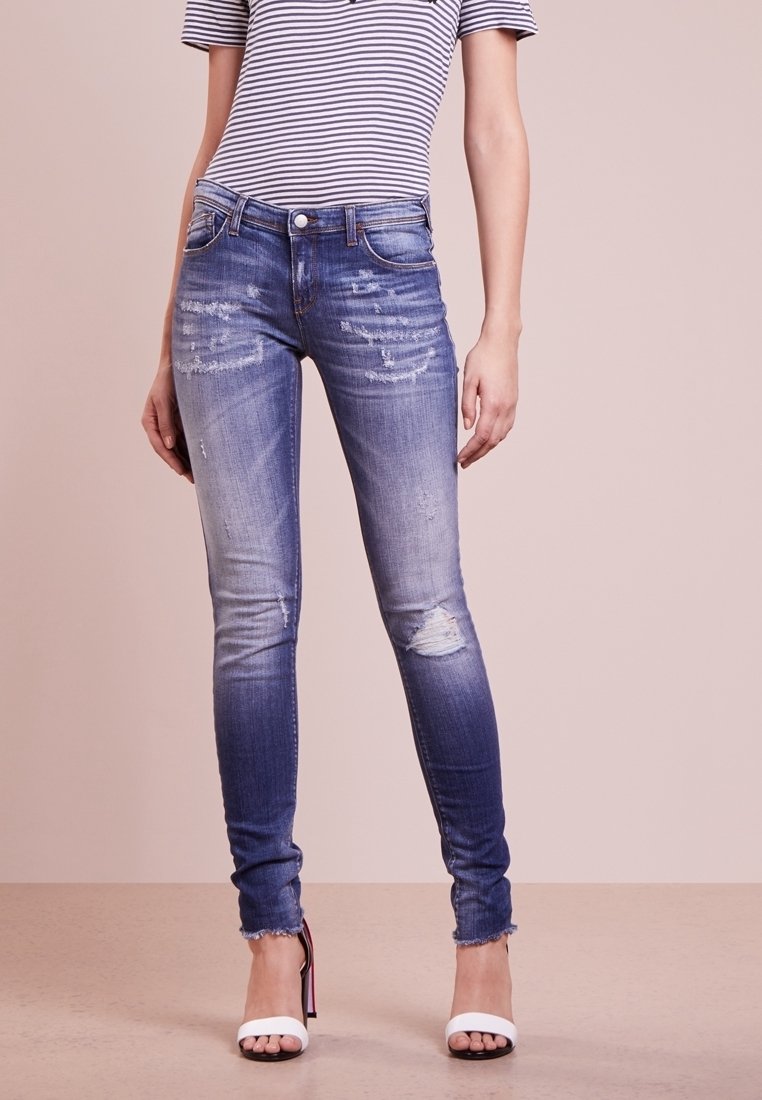 Verblasste blaue Skinny-Jeans aus Baumwollmischung, mit abgetragenen Akzenten und fransigen Säumen, kombiniert mit einem gestreiften Oberteil und offenen Schuhen.