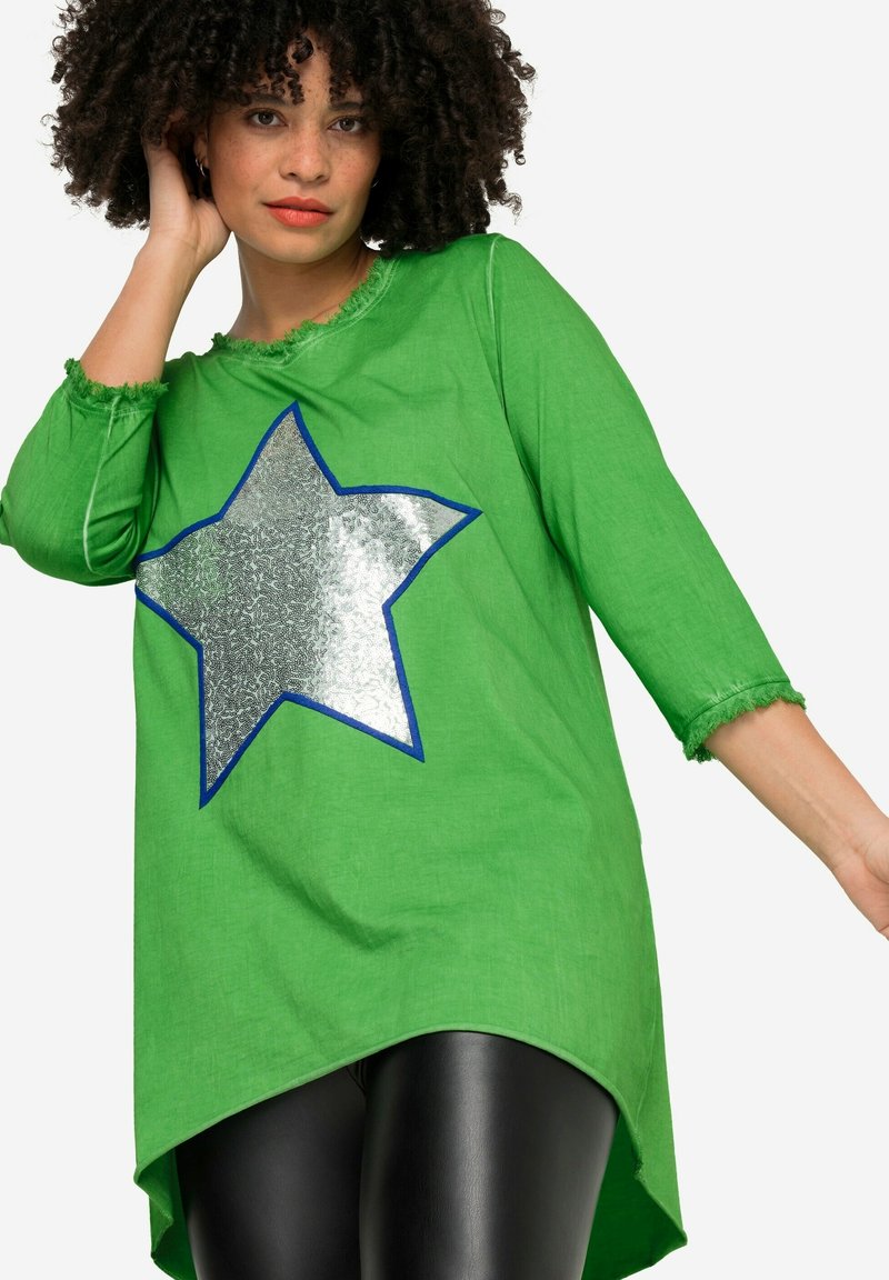 Tunique en coton verte avec un design de star argenté brillant entouré de bleu. Dotée de manches trois-quarts et d'un ourlet arrière plus long.