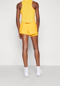 Gelbes Mesh-Top und Shorts-Set mit lockerer Passform und elastischem Bund. Getragen mit weißen Sneakers und Knöchelsocken.