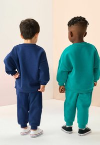 Kaks last, kes kannavad sobivaid üle suuruses pikki pusa ja kitsenevaid vabaaja pükse. Üks tumesinisena, teine laguunrohelisena. Mõlemal valged tossud.