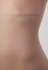 Naadloze naadloze shapewear in huidtint met een soepele textuur, met een diagonale patroon en zonder zichtbare naden langs de taille.