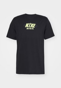 Musta puuvillainen t-paita, jossa on suuri neonkeltaisen "NIKE" -logon ja "JUST DO IT." -tekstin painatus edessä, sekä klassinen pyöreä pääntie.