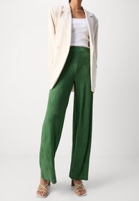 Zelené kalhoty s širokými nohavicemi a vzorem palmových listů, doplněné bílým žebrovaným tílkem a světle béžovým volným sakem. Sandály na tenkých páscích.