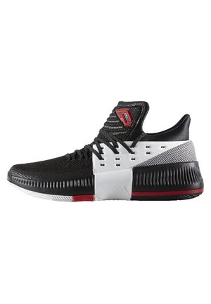 Schwarz-weißer flacher Sportschuh mit schwarzen Schnürsenkeln, rotem Logo auf der Zunge, strukturierter Sohle und roten Akzenten an Sohle und Ferse.