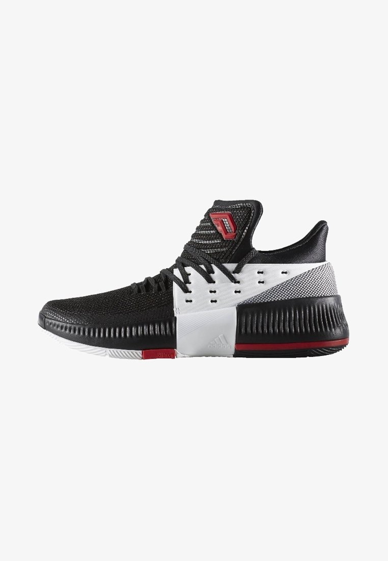 Chaussure de sport basse noire et blanche avec lacets noirs, logo rouge sur la languette, semelle texturée et accents rouges sur la semelle et le talon.