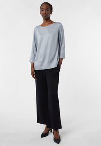 Top satin grigio chiaro con maniche a tre quarti, abbinato a pantaloni neri a gamba larga e tacchi a punta neri, creando una silhouette elegante.