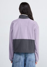 Purple and gray fleece pullover with a high collar, stitched details, and a relaxed fit, shown from the back against a light background.