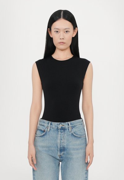 Schwarzer ärmelloser Body mit rundem Ausschnitt und körpernahem Design, kombiniert mit hellblauen, faded High-Waist-Jeans.
