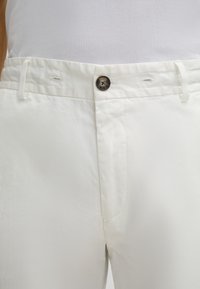 White cotton trousers with a smooth texture, featuring a front button closure, belt loops, and a flat front without pockets.