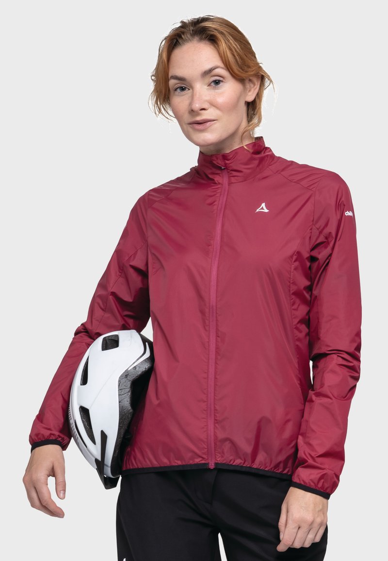 Bordeauxfarbene, leichte Radjacke mit Reißverschluss vorne, hohem Kragen und elastischen Bündchen, gehalten mit einem weißen Helm vor einem neutralen Hintergrund.