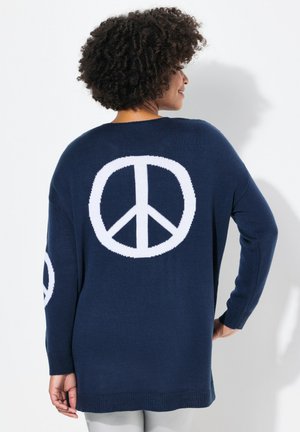 Navyblauwe gebreide trui met grote witte vredessymboolgraphics op de achterkant en mouwen, met een ruime pasvorm en geribde manchetten.