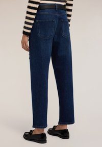 Pantalones de mezclilla en azul oscuro con un diseño de talle alto, bolsillos traseros y un corte recto. Combinados con zapatos negros.