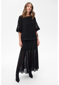 Czarny dwu-elementowy zestaw składający się z przezroczystej bluzki z szerokimi rękawami oraz zwiewnej przezroczystej spódnicy. Teksturowane akcenty na bluzce podkreślają jej wygląd.