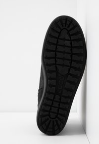 Botte noire avec une semelle en caoutchouc texturée. Présente un motif de bande de roulement robuste pour l'adhérence et une tige en cuir lisse avec peu de détails de couture.