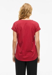 T-shirt rossa in cotone con maniche corte a risvolto, scollatura rotonda e orlo curvo, caratterizzata da una texture liscia e priva di motivi visibili.