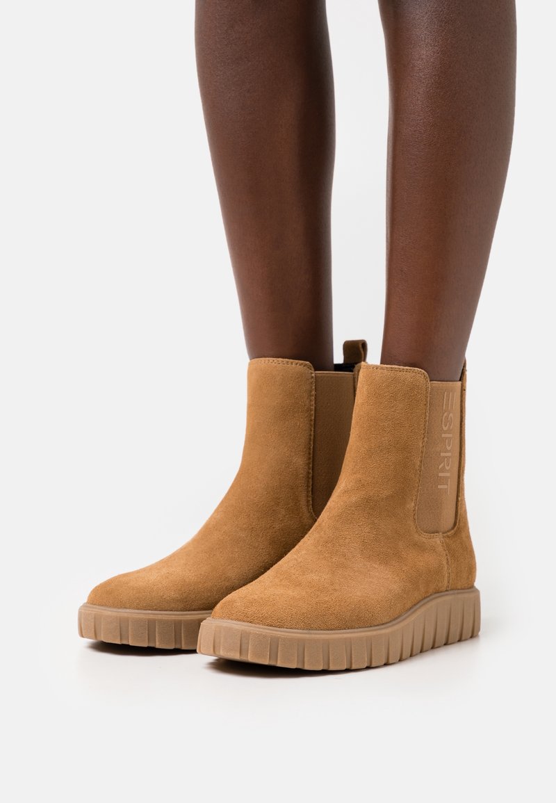 Brązowe zamszowe botki za kostkę z elastycznymi bocznymi panelami, teksturowaną gumową podeszwą i wytłoczonym logo po zewnętrznej stronie.