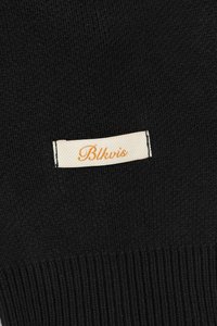 Black knit beanie featuring a textured, ribbed design with a contrasting beige label that reads "Blkvis" in orange cursive lettering.