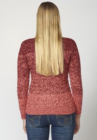 Red ombre knit sweater with a textured pattern, featuring long sleeves and a fitted silhouette, paired with dark blue jeans.