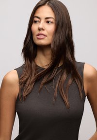 Ciemnoszary, bezrękawnik, prążkowana faktura, okrągły dekolt, gładka tkanina, noszony z luźnymi, falującymi włosami, neutralne tło.