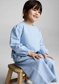 Robe rayée bleu et blanc avec de longues manches bouffantes et un col rond. Tissu doux, design en A, longueur genou, portée par un enfant assis.