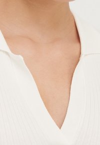 Gros plan sur le cou et le haut de la poitrine d'une personne portant un vêtement blanc à col en V côtelé avec un col.