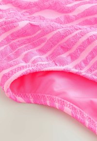 Rosa Schwimmbekleidung mit einem strukturierten, wellenförmigen Design und einem gerafften Rand. Das Innenfutter ist glatt und hat einen lebhaften, einfarbigen Rosaton.