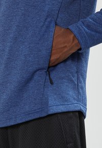 Top blu lungo con maniche, realizzato in tessuto testurizzato, con una tasca laterale con zip e una vestibilità comoda, abbinato a pantaloni corti in rete neri.